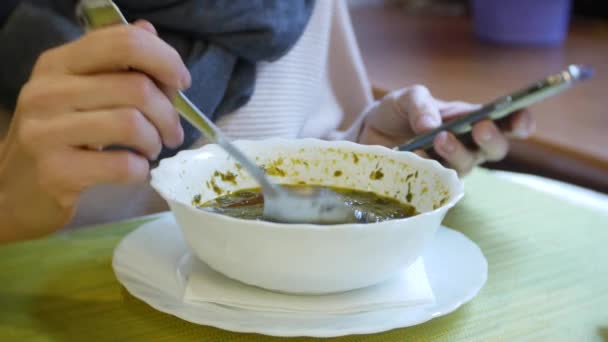 Una mujer está cenando en un café con un teléfono inteligente. 4k — Vídeos de Stock