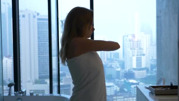 Schöne Frau, die sich in einem luxuriösen Badezimmer mit Fenster mit einem Handtuch abwischt. das Konzept einer Lebensweise und Schönheit. Blick vom Fenster auf die Wolkenkratzer. 4k — Stockvideo