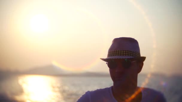 Joven con sombrero y gafas de sol viajando en barco al atardecer. 4k — Vídeo de stock