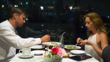 Konuşmaya ve bir barda yemek yerken mutlu çift gökdelenler, akşamları bakan, 4k, arka plan bulanıklık