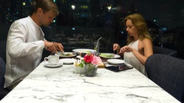 Konuşmaya ve bir barda yemek yerken mutlu çift gökdelenler, akşamları bakan, 4k, arka plan bulanıklık