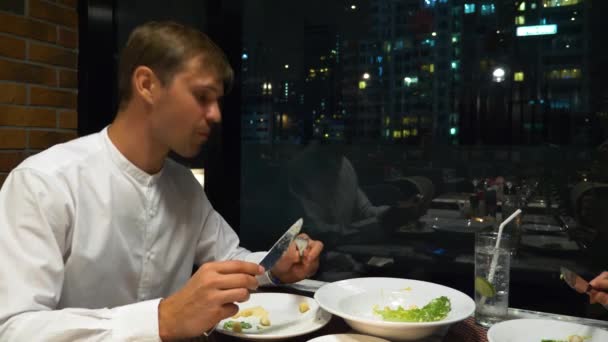 Casal feliz conversando e jantando em um bar com vista para arranha-céus, à noite, 4K, fundo embaçado — Vídeo de Stock