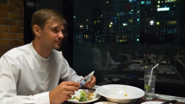 Pareja feliz hablando y cenando en un bar con vistas a los rascacielos, por la noche, 4k, fondo borroso — Vídeos de Stock