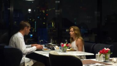 Konuşmaya ve bir barda yemek yerken mutlu çift gökdelenler, akşamları bakan, 4k, arka plan bulanıklık