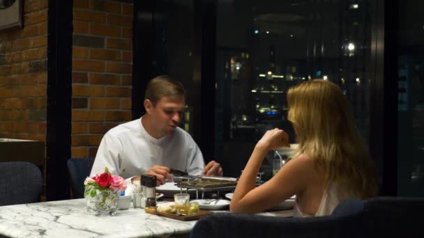 Pareja feliz hablando y cenando en un bar con vistas a los rascacielos, por la noche, 4k, fondo borroso — Vídeos de Stock