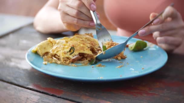 Macarrão de amido frito com frutos do mar em uma omelete. 4k close-up. uma mulher come com uma colher e garfo um prato nacional tailandês . — Vídeo de Stock