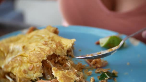 Mezcla fideos de almidón fritos con mariscos en una tortilla. 4k primer plano. una mujer come con una cuchara y tenedor un plato nacional tailandés . — Vídeos de Stock