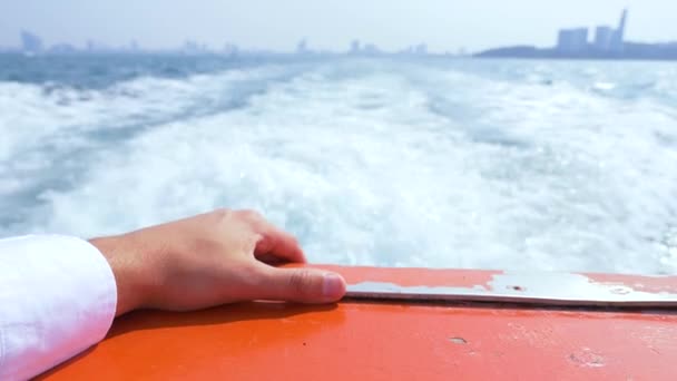 Primer plano de las manos a bordo de un barco. Olas y ciudad moderna en el fondo, cámara lenta, 4k — Vídeos de Stock