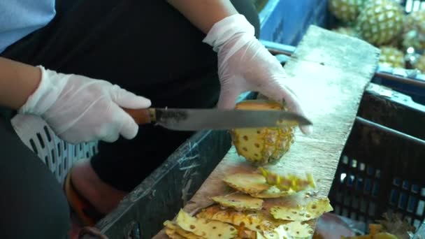 Frauenhände in Gummihandschuhen säubern Ananas auf dem Wochenmarkt. Thailand, Obst. 4k, — Stockvideo