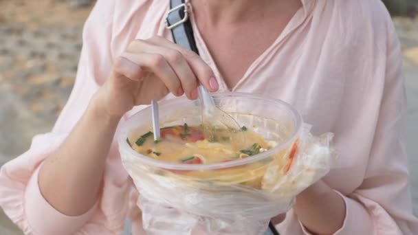 Mujer comiendo sopa tailandesa Tom Yam sentado en la playa, 4k cámara lenta — Vídeos de Stock