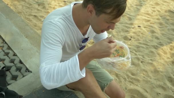 Hombre comiendo sopa tailandesa Tom Yam sentado en la playa, 4k cámara lenta — Vídeos de Stock