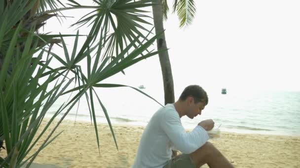 Hombre comiendo sopa tailandesa Tom Yam sentado en la playa, 4k cámara lenta — Vídeos de Stock