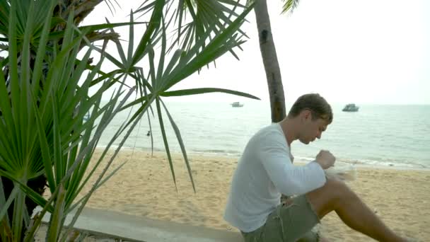 Hombre comiendo sopa tailandesa Tom Yam sentado en la playa, 4k cámara lenta — Vídeos de Stock