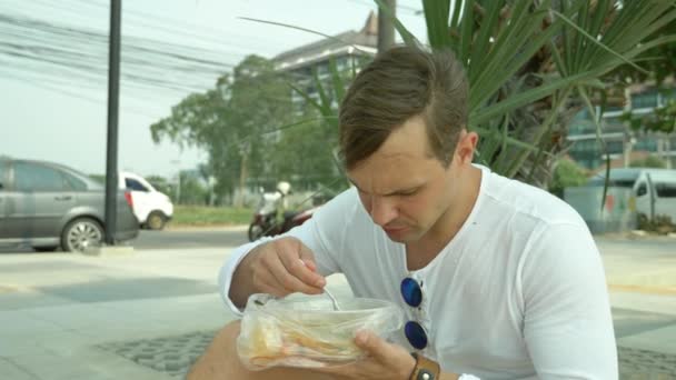 Uomo che mangia zuppa tailandese Tom Yam seduto sulla spiaggia, 4k slow-motion — Video Stock