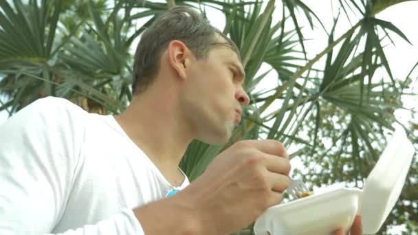 Людина їсть тайський суп Том ям, сидячи на пляжі, 4 к повільному — стокове відео