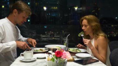 Konuşmaya ve bir barda yemek yerken mutlu çift gökdelenler, akşamları bakan, 4k, arka plan bulanıklık