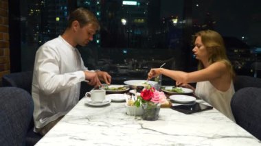 Konuşmaya ve bir barda yemek yerken mutlu çift gökdelenler, akşamları bakan, 4k, arka plan bulanıklık
