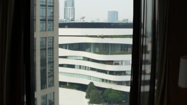 Un hombre feliz en pantalones cortos se encuentra cerca de la ventana después de despertar, vista desde la ventana a los rascacielos. 4k cámara lenta — Vídeos de Stock