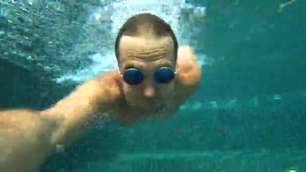Un giovane maschio bianco bello che fa un selfie subacqueo su una action camera. Ritratto di un giovane con gli occhiali che si toglie dalla macchina fotografica sott'acqua. 4k — Video Stock