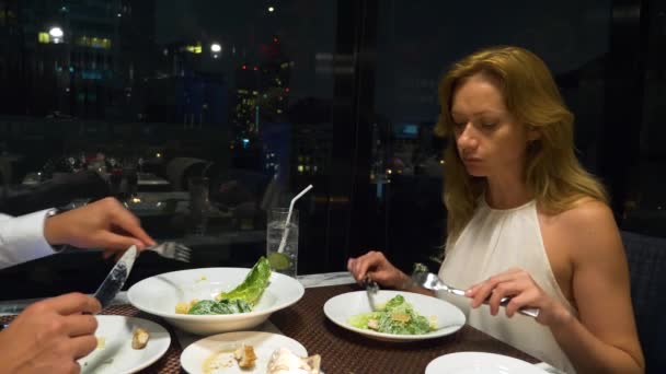 Ευτυχισμένο ζευγάρι μιλάμε και έχοντας το γεύμα σε ένα μπαρ με θέα ουρανοξύστες, το βράδυ, 4k, Θάμπωμα φόντου — Αρχείο Βίντεο