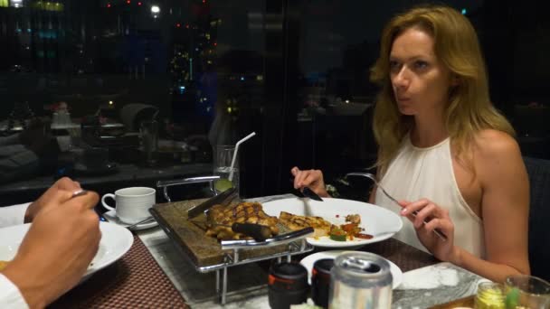 Pareja feliz hablando y cenando en un bar con vistas a los rascacielos, por la noche, 4k, fondo borroso — Vídeos de Stock