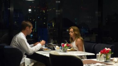 Konuşmaya ve bir barda yemek yerken mutlu çift gökdelenler, akşamları bakan, 4k, arka plan bulanıklık