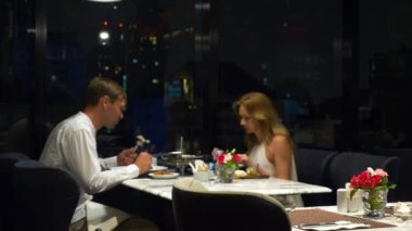 Konuşmaya ve bir barda yemek yerken mutlu çift gökdelenler, akşamları bakan, 4k, arka plan bulanıklık