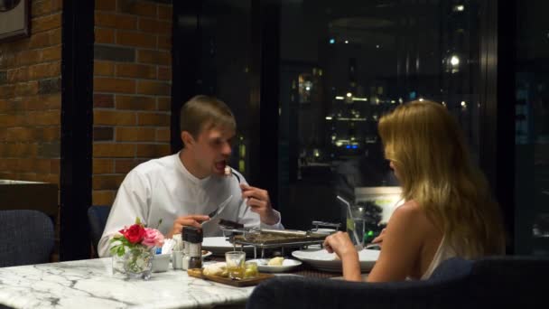 Щаслива пара розмовляє і вечеряє в барі з видом на хмарочоси, ввечері, 4k, розмитий фон — стокове відео