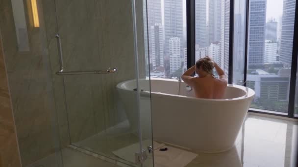 Mooie vrouw, wassen van haar haren in een luxe badkamer met een venster. Het concept van een manier van leven en schoonheid. uitzicht vanaf het venster naar de wolkenkrabbers. 4k — Stockvideo