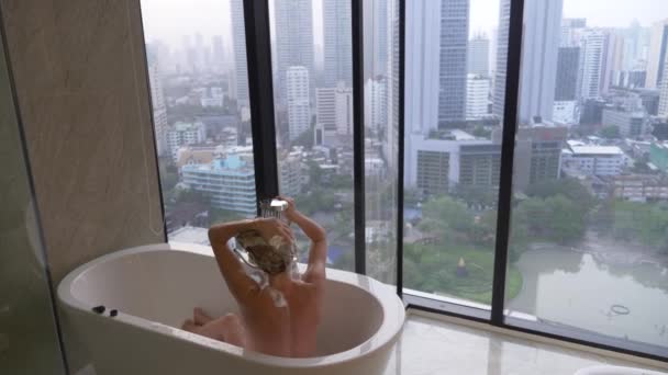 Krásná žena myje vlasy v luxusní koupelnu s oknem. Koncept způsobu života a krásy. pohled z okna na mrakodrapy. 4k