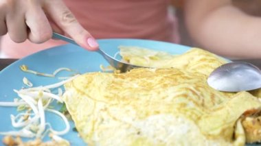 Omlet deniz ürünleri ile tavada kızartılmış nişasta erişte. 4 k yakın çekim. bir kadın bir kaşık ve çatal Tayland ulusal yemek yiyor.
