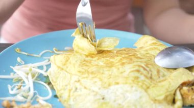 Omlet deniz ürünleri ile tavada kızartılmış nişasta erişte. 4 k yakın çekim. bir kadın bir kaşık ve çatal Tayland ulusal yemek yiyor.