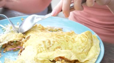Omlet deniz ürünleri ile tavada kızartılmış nişasta erişte. 4 k yakın çekim. bir kadın bir kaşık ve çatal Tayland ulusal yemek yiyor.