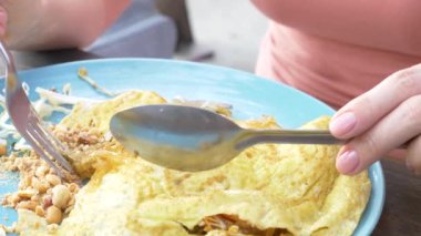 Omlet deniz ürünleri ile tavada kızartılmış nişasta erişte. 4 k yakın çekim. bir kadın bir kaşık ve çatal Tayland ulusal yemek yiyor.