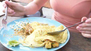 Omlet deniz ürünleri ile tavada kızartılmış nişasta erişte. 4 k yakın çekim. bir kadın bir kaşık ve çatal Tayland ulusal yemek yiyor.