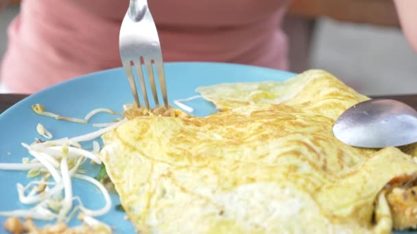 Nouilles à l'amidon frit avec fruits de mer dans une omelette. Plan rapproché 4k. une femme mange avec une cuillère et fourchette un plat national thaïlandais . — Video