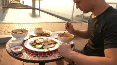Karides çorbası ekşi ve baharatlı tadı ile Tay bir yemektir. adam Tom Yam havuzun yanında bir masada yiyor. 4 k, ağır çekim, yakın çekim. Turizm turizm kavramı