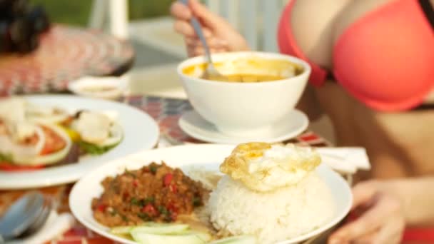 Kryddig räksoppa är en thailändsk maträtt med syrlig och kryddig smak. Busty flicka i en bikini äter Tom Yam vid ett bord vid poolen. 4 k, slow motion, närbild. begreppet resor turism — Stockvideo