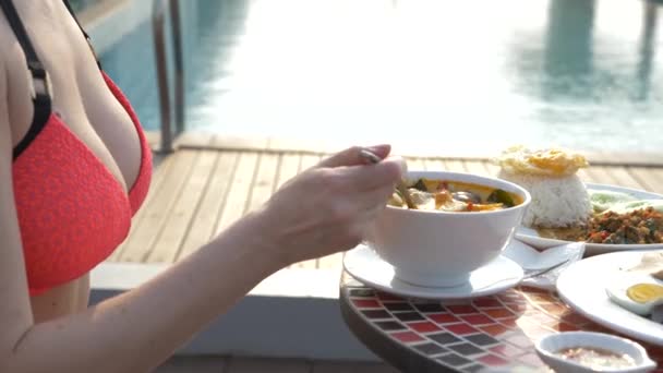 La sopa picante de gambas es un plato tailandés con sabor agrio y picante. chica tetona en bikini come Tom Yam en una mesa junto a la piscina. 4k, cámara lenta, primer plano. concepto de turismo de viaje — Vídeos de Stock