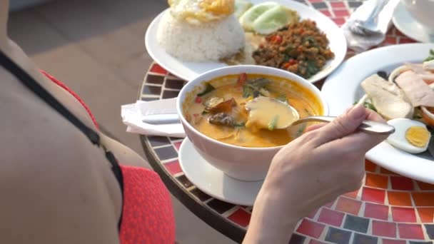 Zuppa di gamberetti piccante è un piatto tailandese con sapore aspro e piccante. ragazza tettona in bikini mangia Tom Yam a un tavolo a bordo piscina. 4K, rallentatore, primo piano. concetto di turismo di viaggio — Video Stock