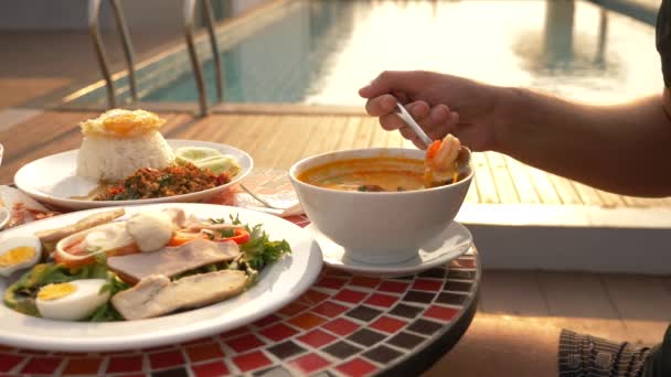 Krevety polévka je thajské jídlo s kyselé a pikantní chuť. muž jí Tom Yam u stolu u bazénu. 4 k, Zpomalený pohyb, detail. pojem turistika Turistika — Stock video