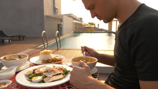 Garnelensuppe ist ein thailändisches Gericht mit saurem und würzigem Geschmack. Der Mann isst Tom Yam an einem Tisch am Pool. 4k, Zeitlupe, Nahaufnahme. Konzept des Tourismus — Stockvideo