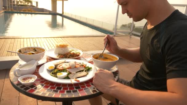 La soupe de crevettes est un plat thaïlandais au goût aigre et épicé. l'homme mange Tom Yam à une table près de la piscine. 4k, ralenti, gros plan. concept de tourisme touristique — Video