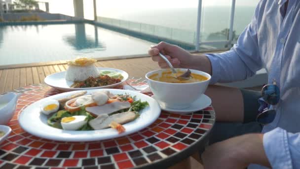 La sopa de camarones es un plato tailandés con un sabor agrio y picante. El hombre se está comiendo a Tom Yam en una mesa junto a la piscina. 4k, cámara lenta, primer plano. concepto de turismo turístico — Vídeo de stock