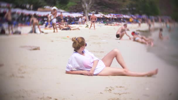 Een doordachte, treurige vrouw, zit alleen op het zand in een overvol strand, 4k, slow-motion. achtergrond vervagen — Stockvideo