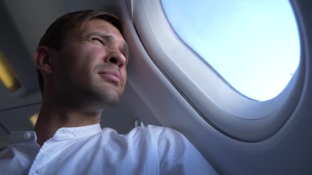 4k, Nahaufnahme. Porträt eines gutaussehenden jungen Mannes, der während des Fluges auf das Flugzeugfenster blickt. — Stockvideo