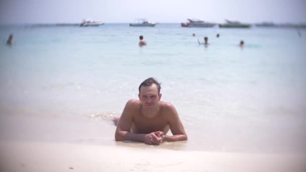 4k, Zpomalený pohyb, mladý muž leží na bílý písek, při pohledu na fotoaparát a usmívá se — Stock video