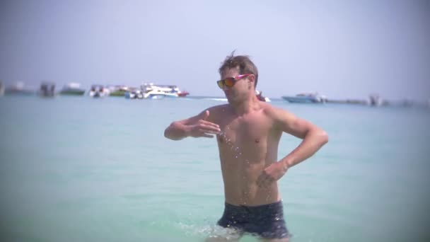 4k, повільний рух, молодий чоловік танцює в морі в окулярах бризкає воду і посміхається — стокове відео