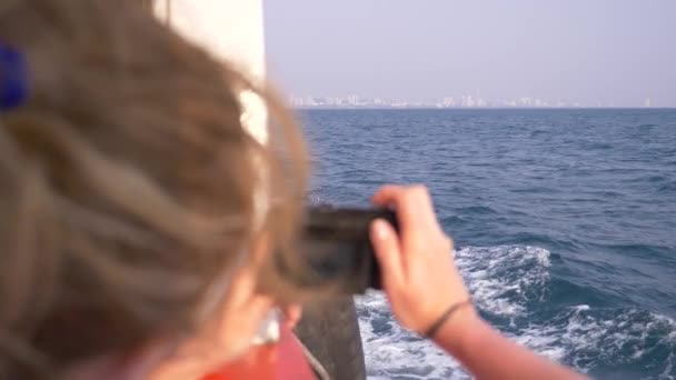 Een mooie vrouw staat op de achtersteven van het schip en maakt een video op de camera. Golven op de achtergrond, slow motion, 4k — Stockvideo