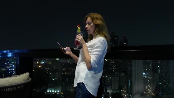 Młoda kobieta Blondynka relaks i picia koktajl w barze z widokiem na wieżowce w nocy. 4k, rozmycie tła — Wideo stockowe